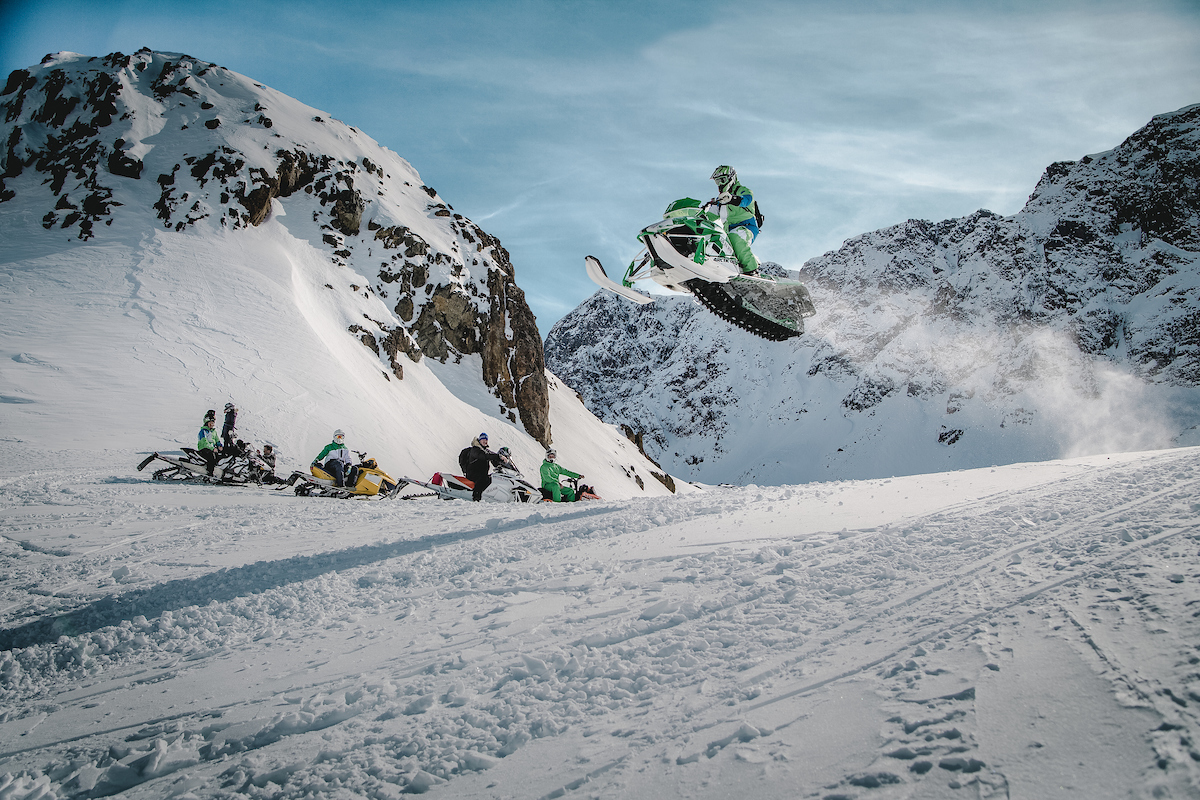 A Snowmobiler Flying High Over A Group Of Friends In The Sisimiut Backckountry In Greenland